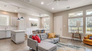 A spacious living area with a gray sectional sofa, a wooden dining table, and a kitchen area with white cabinets and a large window. - 2 Mi to Dtown: Convenient Houston Home! (Houston)