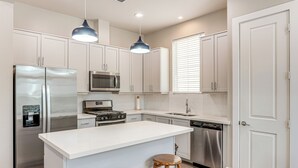 A modern kitchen with white cabinets, stainless steel appliances, a central island with stools, and pendant lighting. - 2 Mi to Dtown: Convenient Houston Home! (Houston)