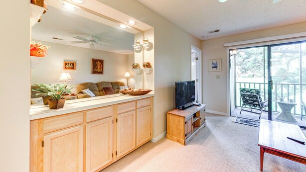 A living room with a TV, wooden cabinets, a sofa, and a balcony with outdoor furniture. - Little River Condo w/ Pool Access: 5 Mi to Beach (Little River)