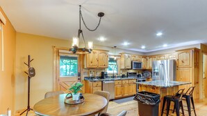 A modern kitchen with wooden cabinets, stainless steel appliances, and a dining area with a round table and chairs. - Deck & Private Hot Tub: Cabin in Ellijay! (Ellijay)