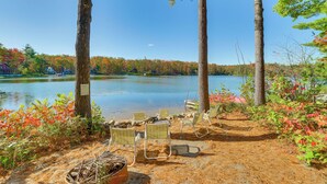 A lakeside campsite with chairs and a fire pit, surrounded by trees and autumn foliage. - Deck & Fire Pit: Near ATV Trails in Gaylord (Gaylord)