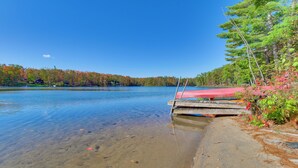 A calm lake with a wooden dock extending into the water, surrounded by autumn-colored trees and a clear blue sky. - Deck & Fire Pit: Near ATV Trails in Gaylord (Gaylord)