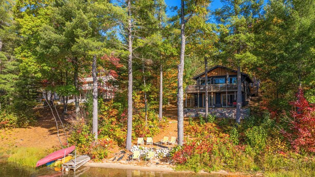 A cabin with a deck overlooking a lake, surrounded by trees and autumn foliage. - Deck & Fire Pit: Near ATV Trails in Gaylord (Gaylord)