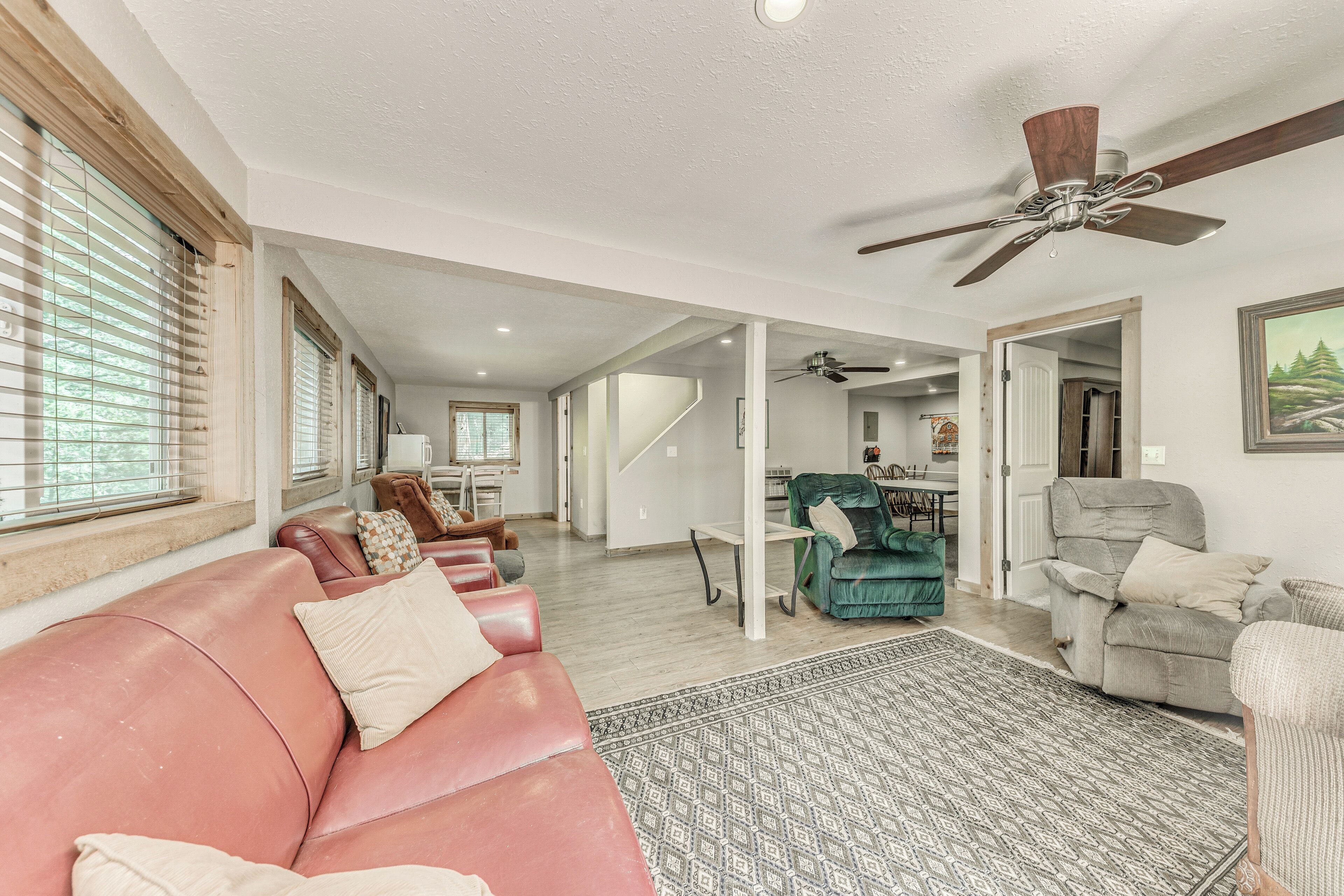 A spacious living room with a red leather couch, a patterned rug, and a ceiling fan.
