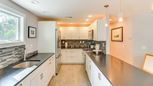 A modern kitchen with white cabinets, a black countertop, and a window providing natural light. - Coastal-modern Home < 3 Mi to Charlestown Beach! (South Kingstown)