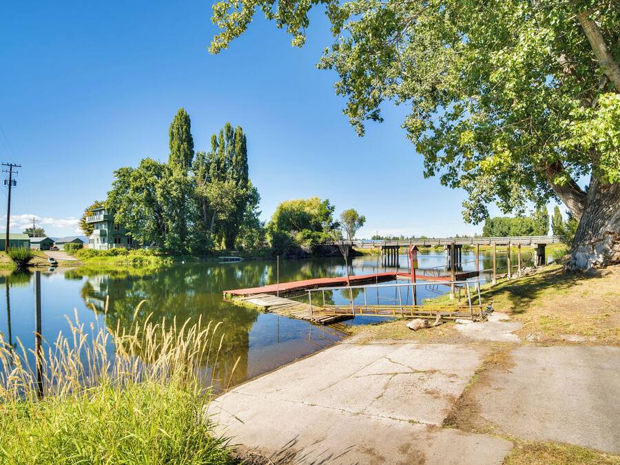 A riverside view with a wooden dock, a bridge, and a building with a green roof.