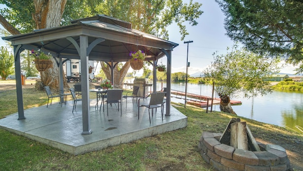 A covered outdoor seating area with chairs and tables, a fire pit, and a view of a lake. - 'crater Lake' Williamson River Resort Cabin 1 (Chiloquin)