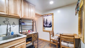 A kitchen with wooden cabinets, a sink, a coffee bar, and a dining area with a chair and table. - 'crater Lake' Williamson River Resort Cabin 1 (Chiloquin)
