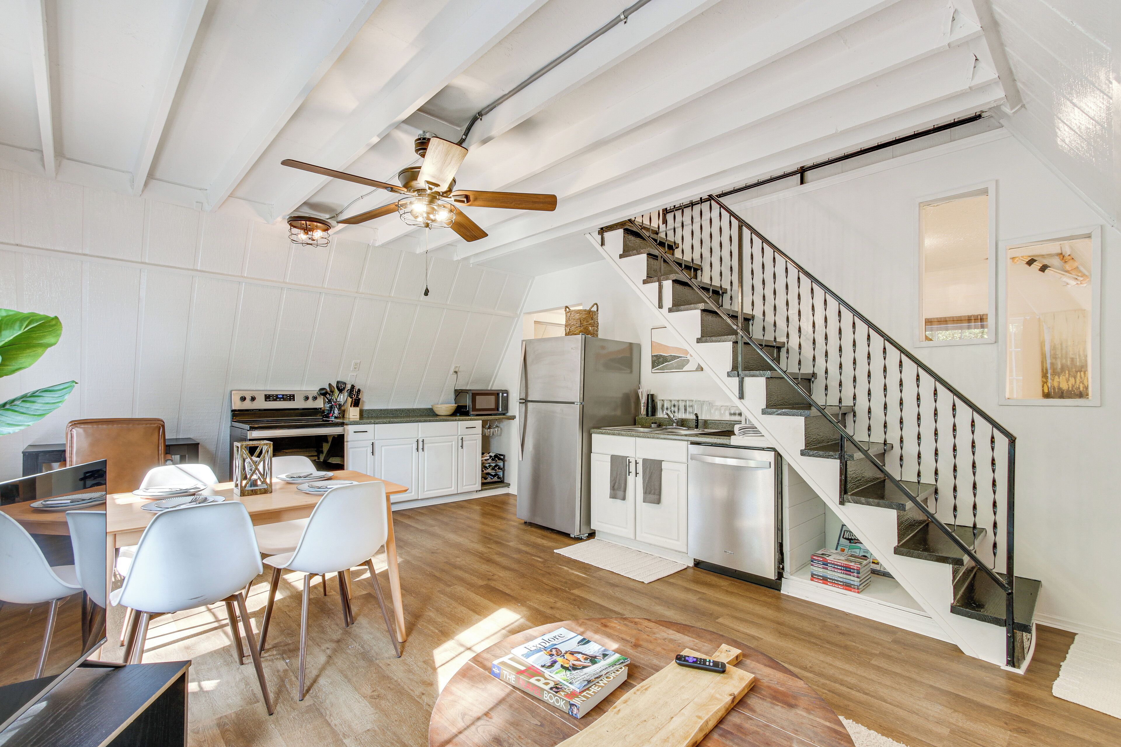 A spacious kitchen with white cabinets, a wooden dining table, and a modern ceiling fan.