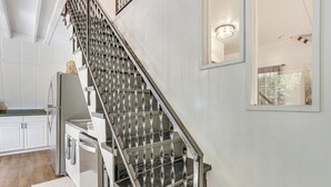 A staircase with a metal railing and a kitchen area with white cabinets and a refrigerator. - A-frame Home ~ 6 Mi to Tennessee River! (Florence)