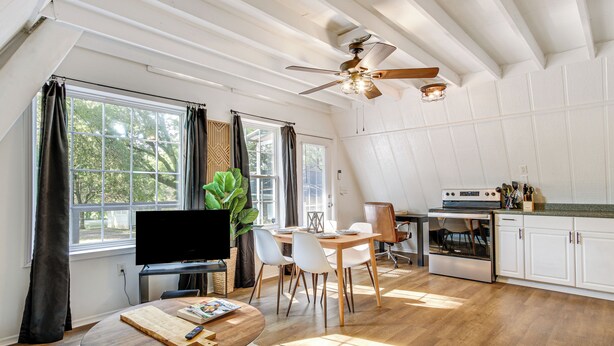 A spacious living area with a dining table, chairs, a TV, and a kitchen area with cabinets and appliances. - A-frame Home ~ 6 Mi to Tennessee River! (Florence)
