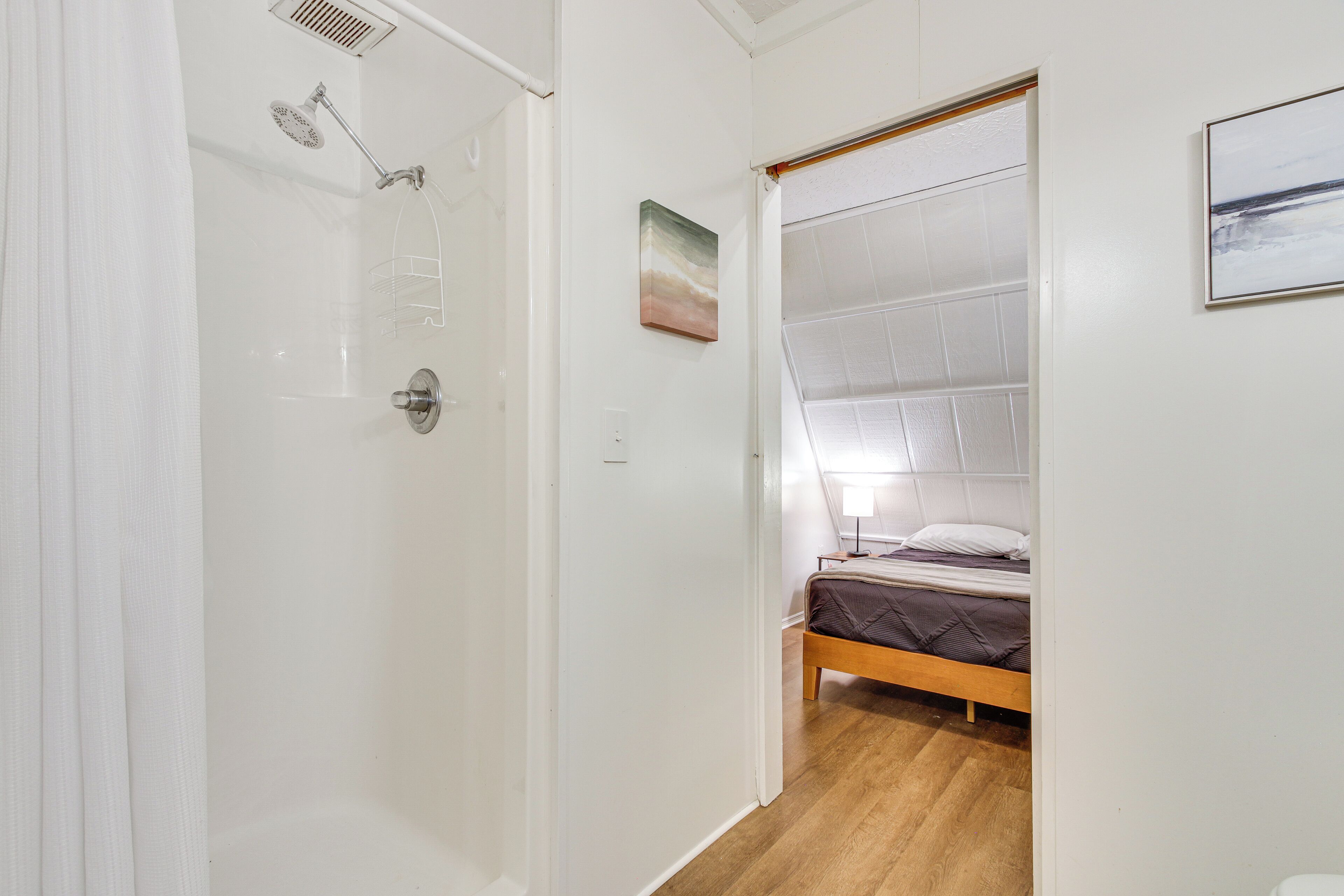 A bedroom with a wooden bed, a shower with a glass door, and a small window.