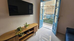 A living room with a TV mounted on the wall, a wooden console table with plants, and a blue door leading to an outdoor balcony. - Cozy Modern two Bdr Place Sliema Ferry Tigne Point (Sliema)