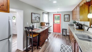 A kitchen with wooden cabinets, a red door, and a stainless steel sink. - 'grandma Kellys' Southeast Indiana Farmhouse! (Cedar Grove)