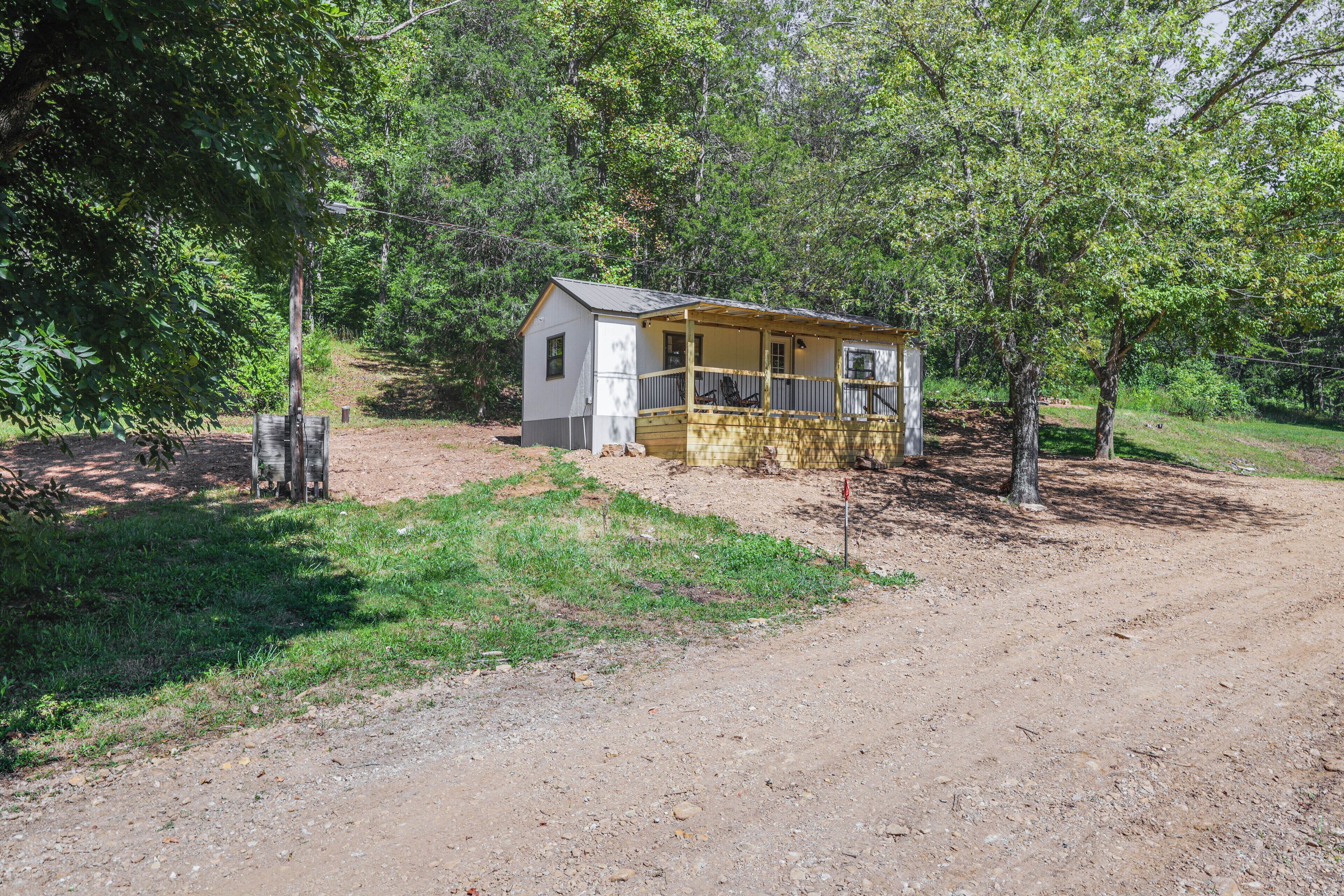 A small, single-story cabin with a porch, surrounded by trees and a dirt path.