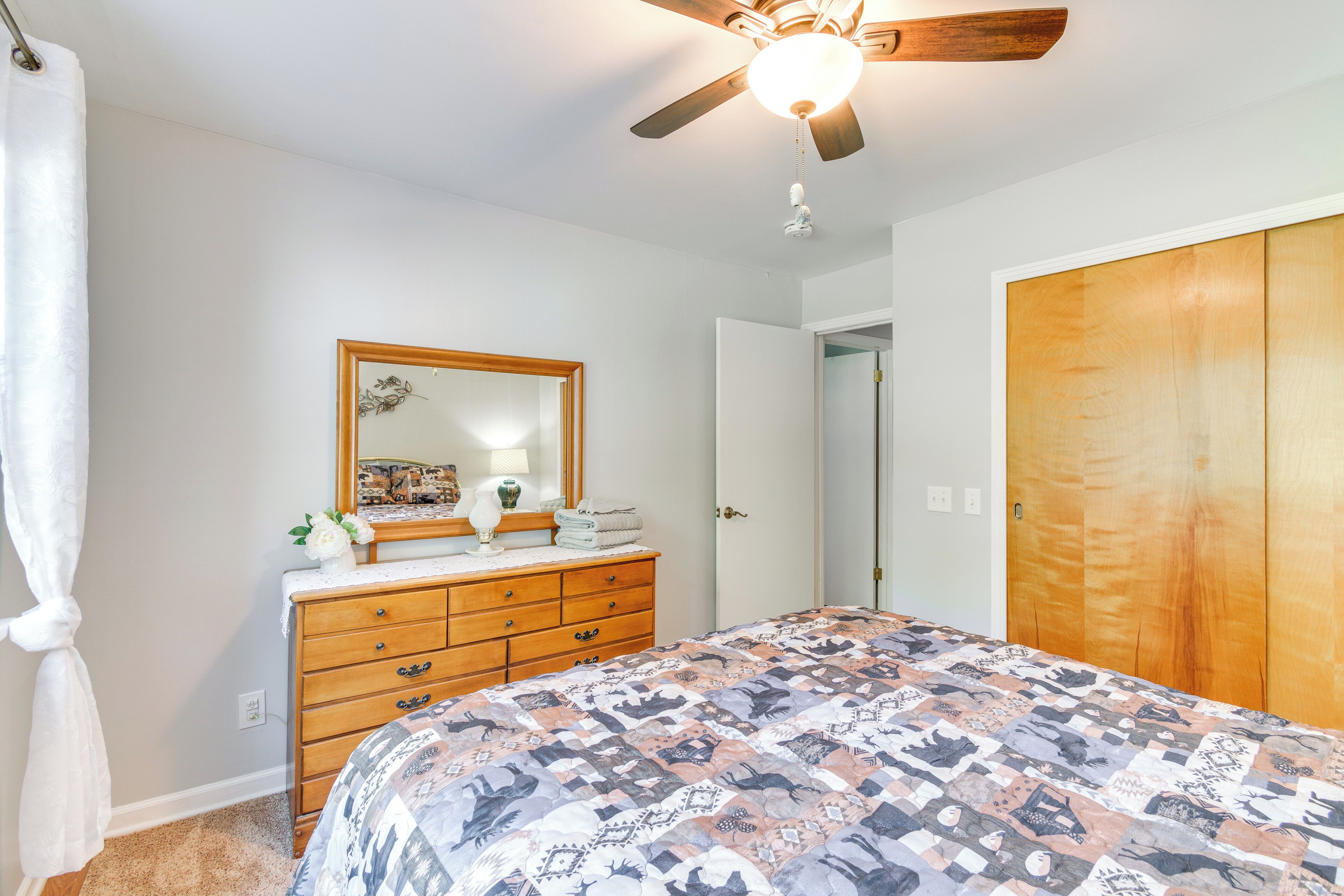 A bedroom with a bed, dresser, mirror, ceiling fan, and wardrobe.