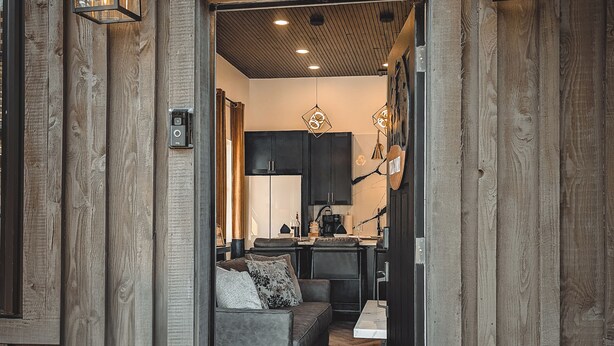 Une façade en bois avec une porte donnant sur un intérieur moderne comprenant un canapé, un coin repas et une cuisine.