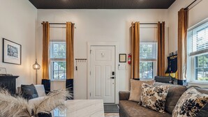 Un salon moderne avec un canapé, une table basse et une cheminée. On y trouve une porte avec un porte-manteau et un tableau encadré accroché au mur.