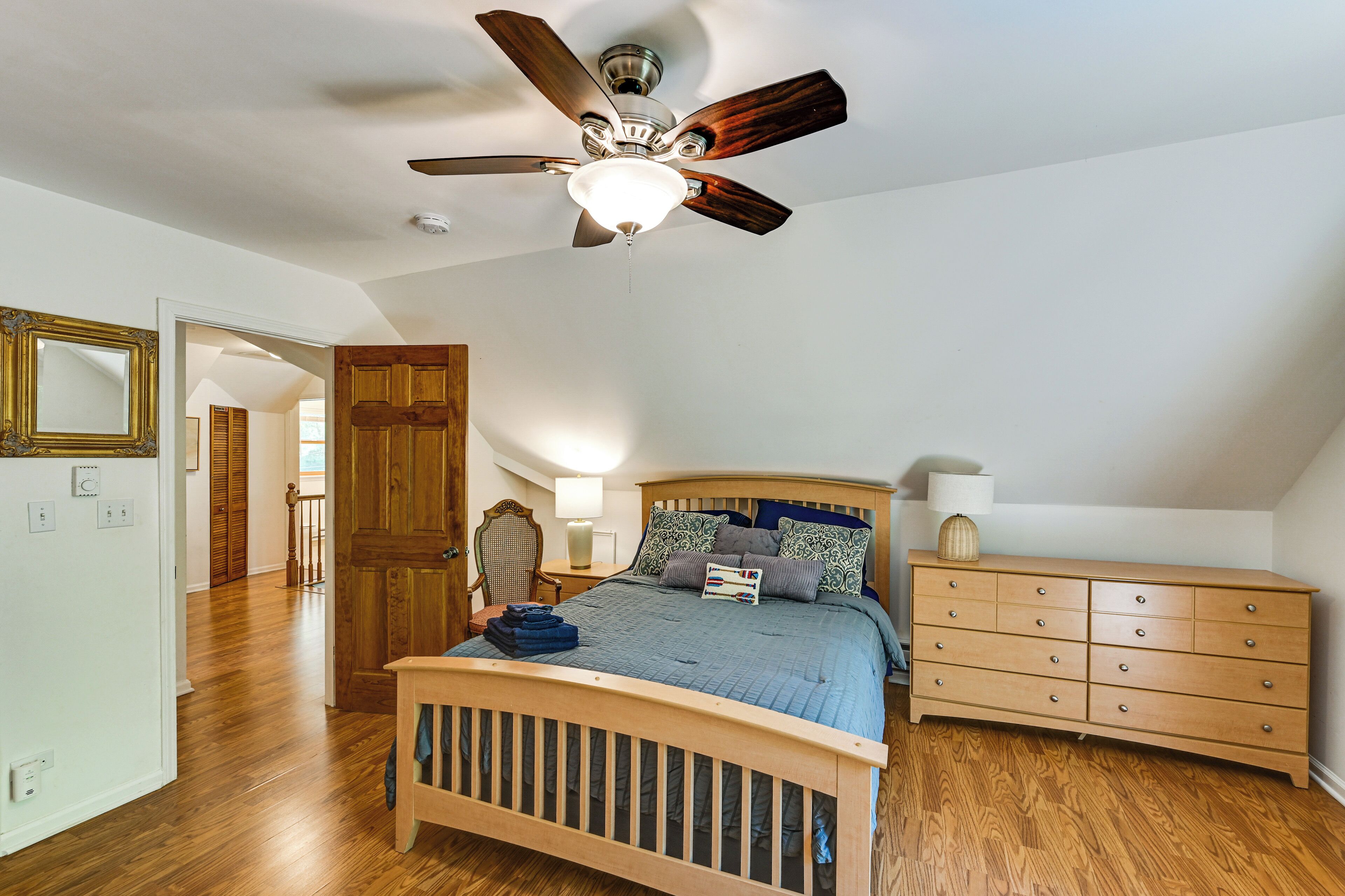 A bedroom with a wooden bed, a ceiling fan, a dresser, and a nightstand.