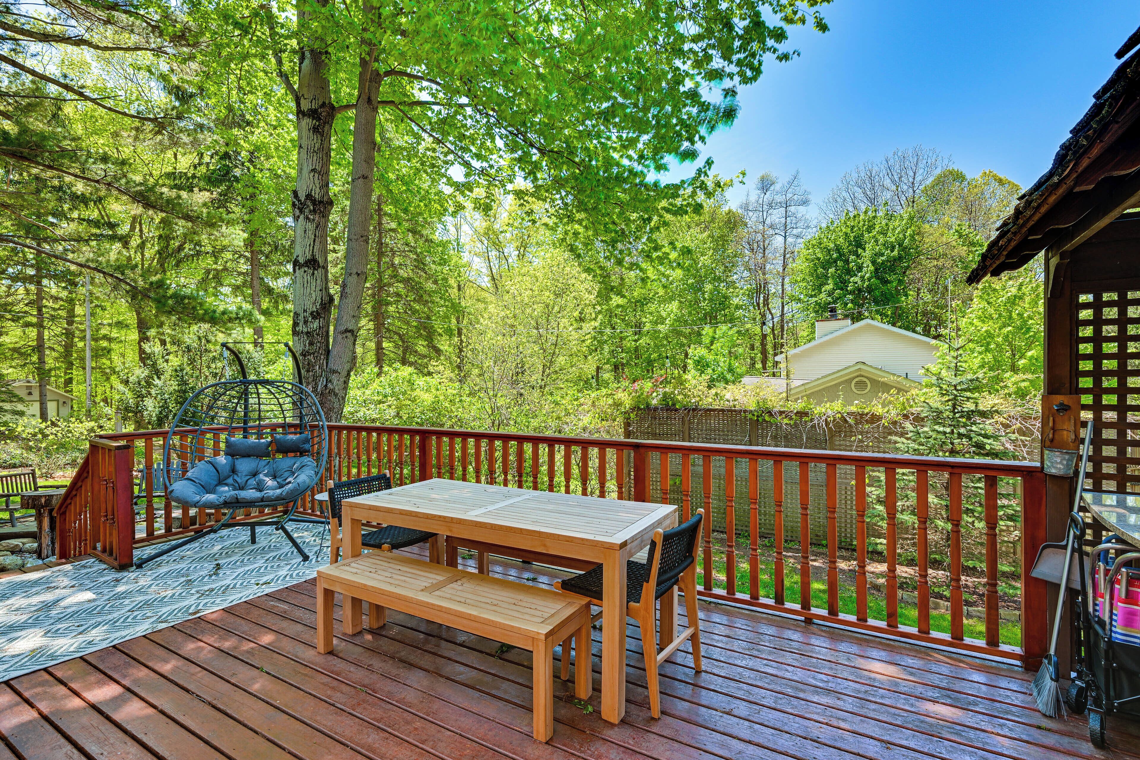 Une terrasse en bois, agrémentée d’une table et de chaises, entourée d’une rambarde rouge, et offrant une vue sur une zone boisée.