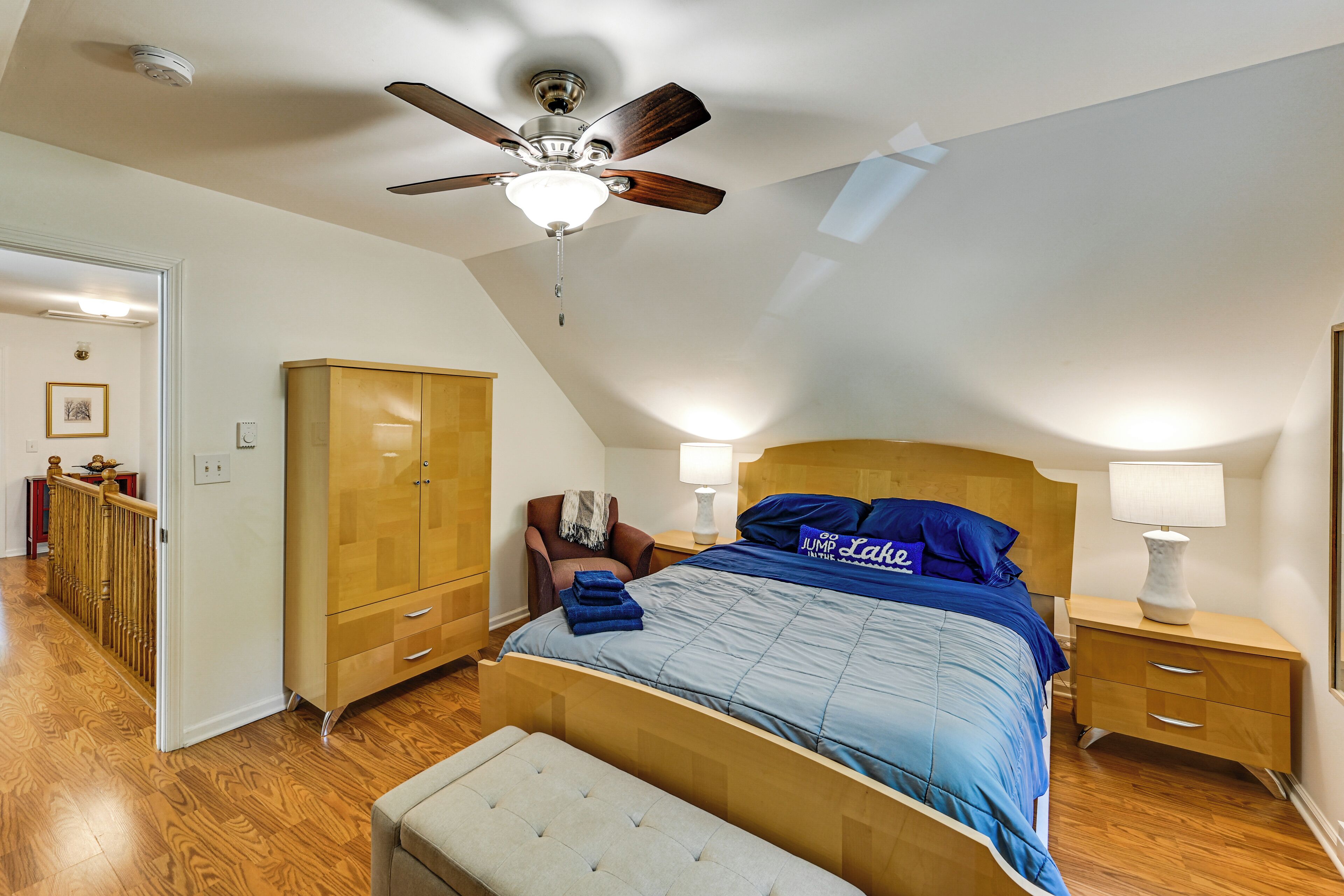 A bedroom with a bed, a ceiling fan, a wardrobe, a nightstand, and a bench.