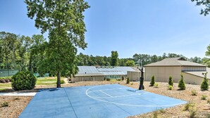 Una cancha de baloncesto al aire libre con superficie azul, rodeada de árboles y un edificio con techo inclinado.