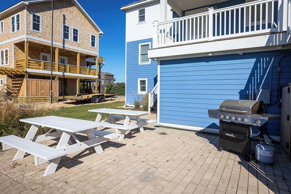 A wooden house with a balcony, a barbecue grill, and picnic tables.