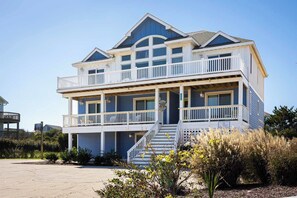 A two-story beachfront house with a balcony, a staircase, and a sign indicating a restaurant.