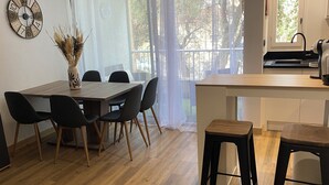 A modern kitchen with a wooden table and chairs, a sink, and a window with a view of trees. - Agréable Appartement de Type F3 (Argelès-sur-Mer)