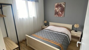 A bedroom with a bed, bedside tables, a nightstand, a wooden shelf, and a window with curtains. - Agréable Appartement de Type F3 (Argelès-sur-Mer)