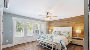 A bedroom with a wooden floor, a bed with a floral bedspread, a ceiling fan, and a nightstand with a lamp. - 39 Oak Court: Sea Pines Luxury! 5 BR, 5.5 BA Private Pool & Spa, Bikes (Hilton Head Island)