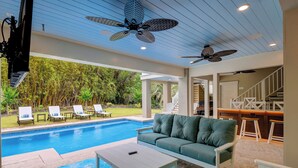 A poolside area with a sofa, a table, and ceiling fans. - 39 Oak Court: Sea Pines Luxury! 5 BR, 5.5 BA Private Pool & Spa, Bikes (Hilton Head Island)