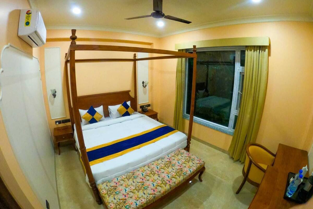 Una cama con dosel, un banco floral, un escritorio con una silla y una ventana con cortinas.