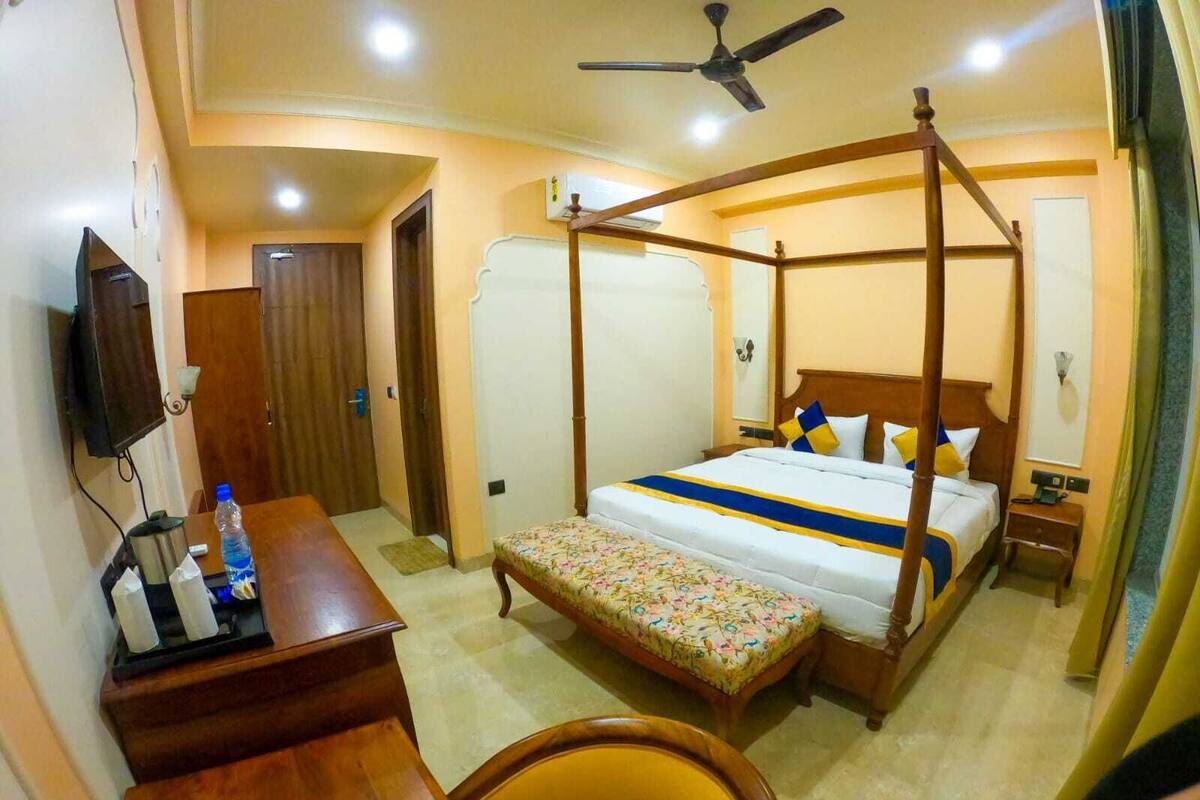 Habitación de hotel con cama con dosel, un escritorio con silla, televisor y ventilador de techo.