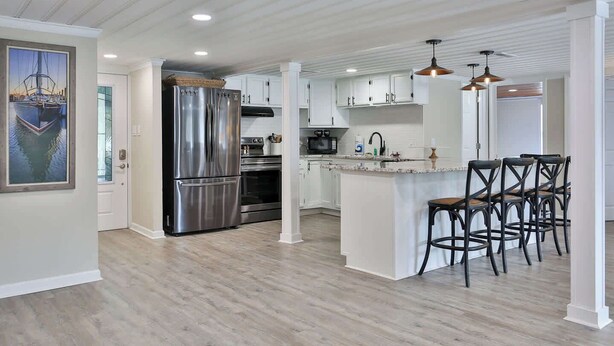 A modern kitchen with stainless steel appliances, white cabinetry, and a bar area with stools. - The Clubhouse Murrells Inlet (Murrells Inlet)