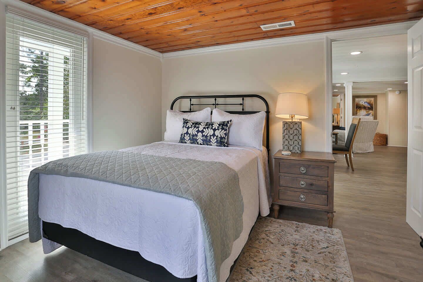 A bedroom with a bed, bedside table, lamp, and a view of the hallway.