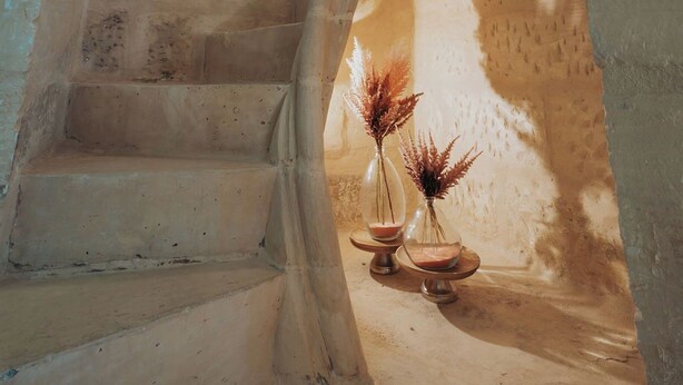 Una escalera de caracol con una pared de piedra rústica y una pequeña mesa con dos jarrones de vidrio al pie.