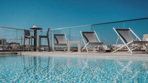 Piscina en la azotea con sillones de descanso y una mesa, con vistas a un paisaje urbano.