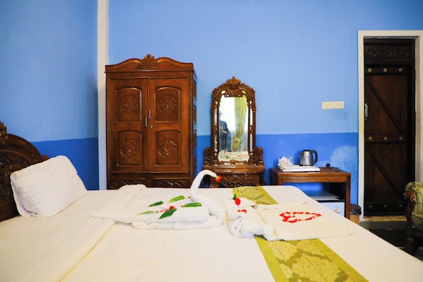 A hotel room with a bed, a wooden wardrobe, a mirror, a small table with a kettle, and a door. - Hill Fort Hotels & Resorts (Tirupattur)