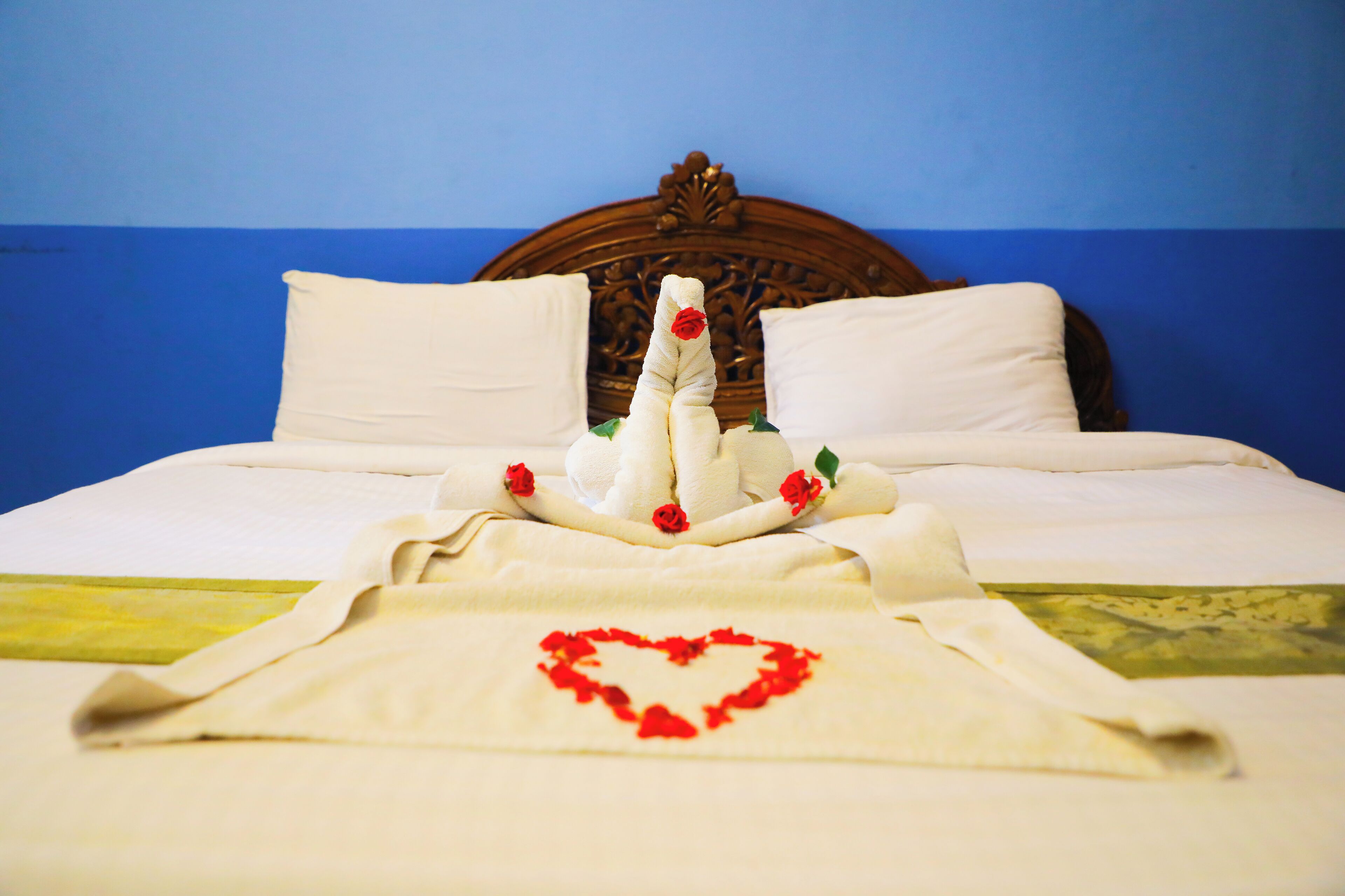 Een bed met een netjes opgevouwen handdoek en rozen decoraties, een hartvormig ontwerp op de spreideken, en een houten hoofdbord.
