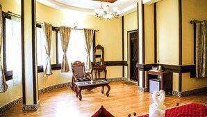 Una habitación amplia con piso de madera, una cama roja, una silla de madera, una mesita y un espejo.
