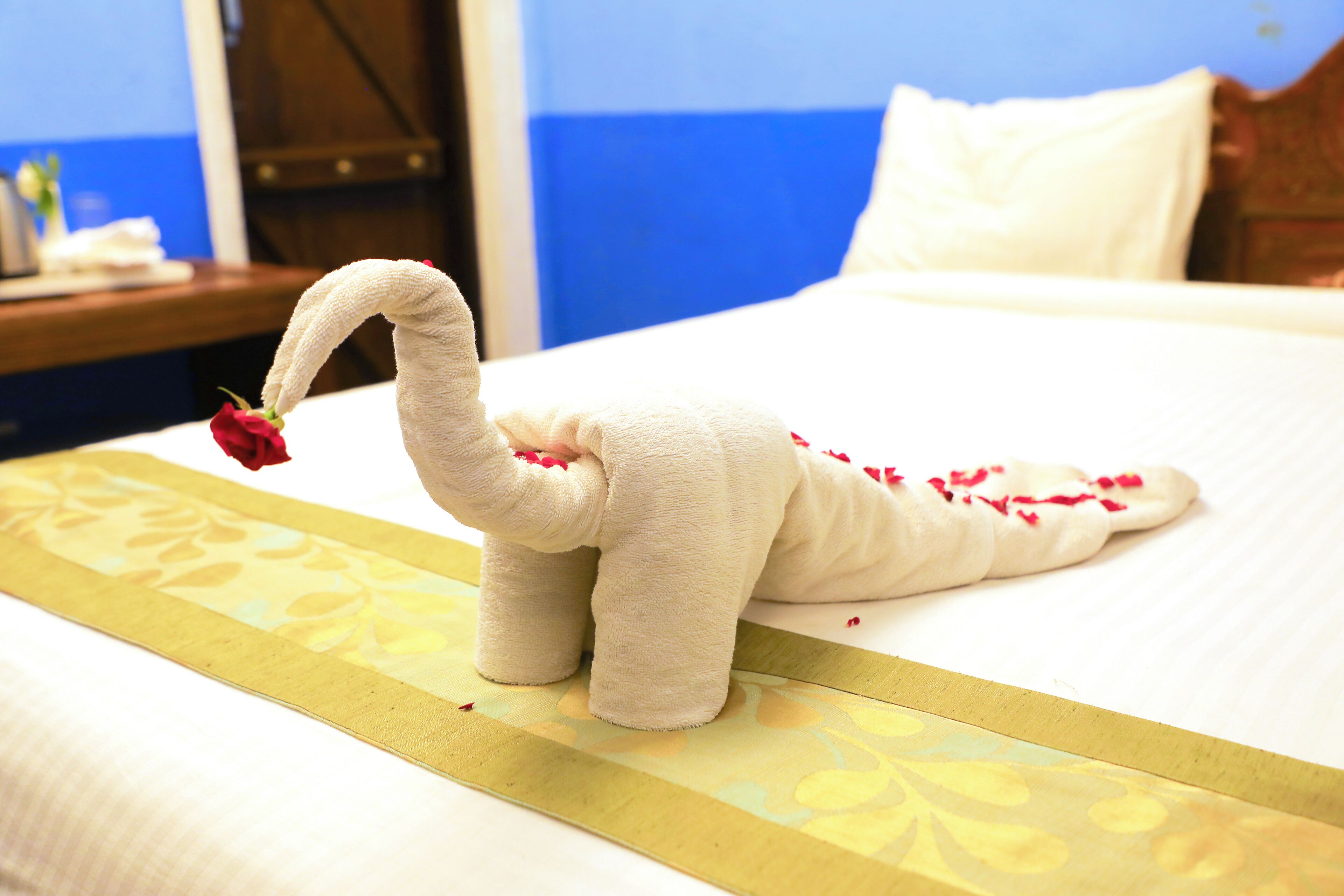 A bed with a decorative towel sculpture resembling a swan, a red rose, and scattered rose petals.
