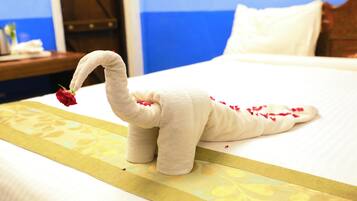 A bed with a decorative towel sculpture resembling a swan, a red rose, and scattered rose petals.