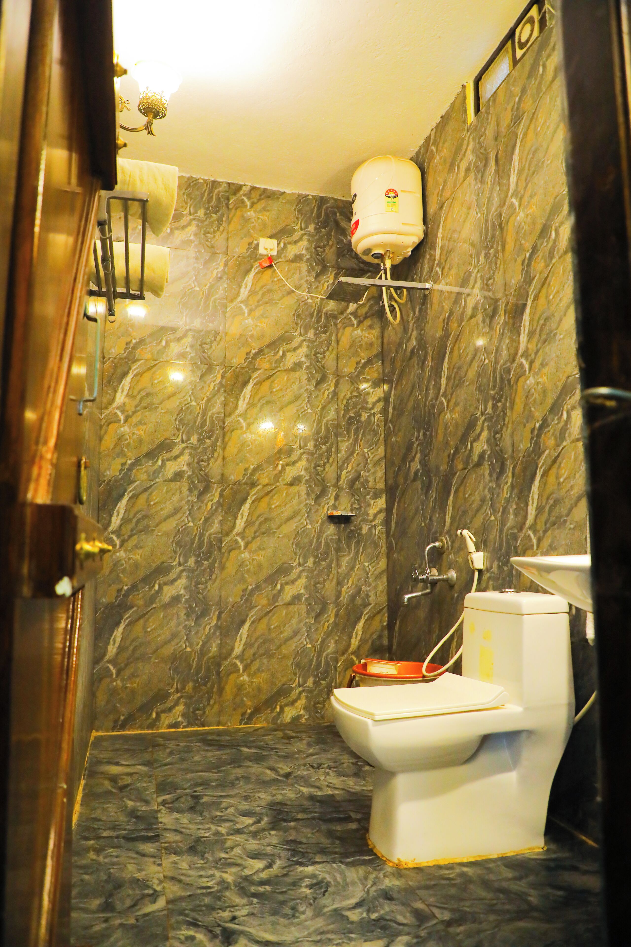 A bathroom with a marble wall, a toilet, a shower, and a towel rack.