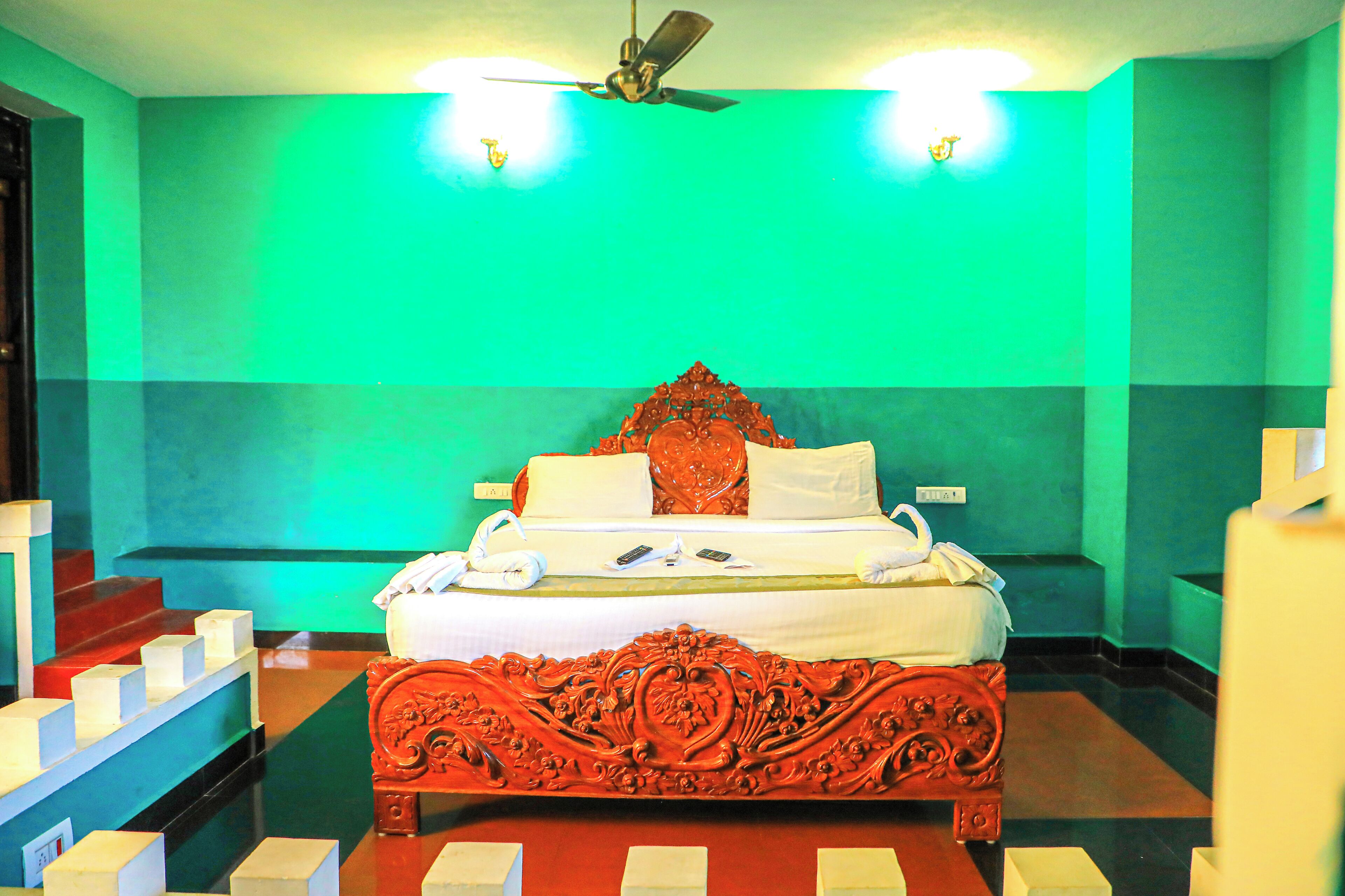 A hotel room with a large ornate bed, a ceiling fan, and a green wall.