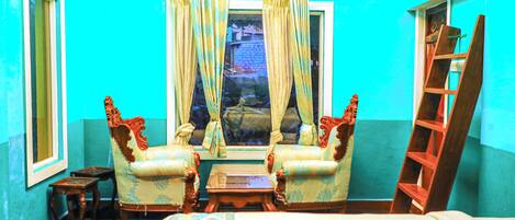 A room with a bed, two armchairs, a small table, a window with curtains, and a wooden ladder.