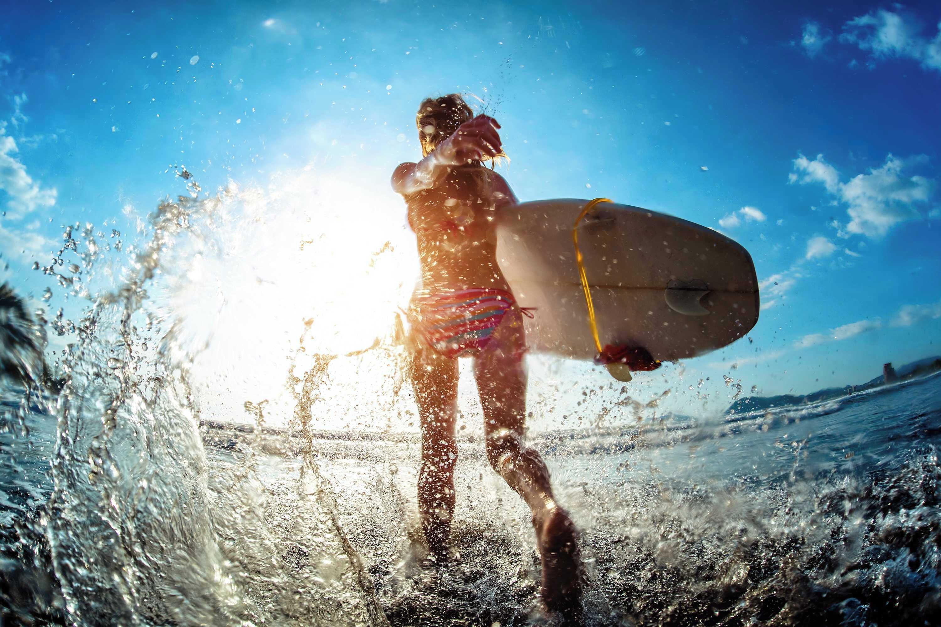 A person holding a surfboard at the beach with the sun shining.