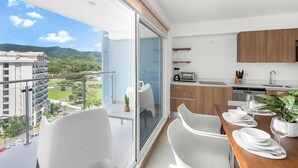 Une cuisine moderne avec un coin repas, une vue sur la ville et un balcon équipé d’une table et de chaises.