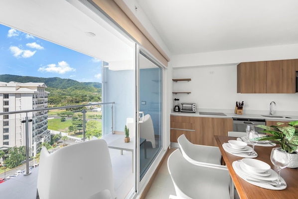 A modern kitchen with a dining area, a view of the city, and a balcony with a table and chairs.