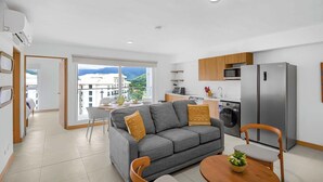 Eine moderne Wohnung mit grauem Sofa, Esstisch aus Holz und Küchenzeile inklusive Kühlschrank und Mikrowelle.